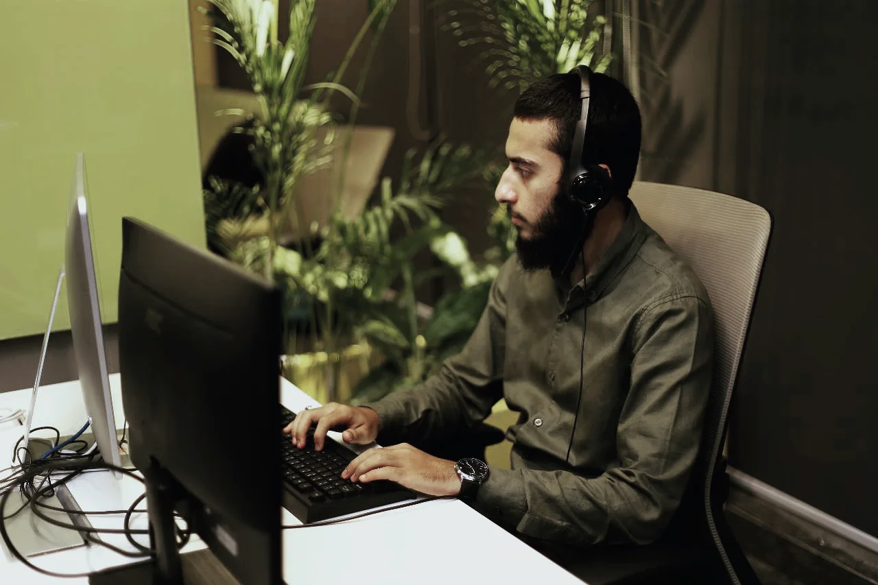 Hunain at his desk with a headset on, working at two screens